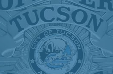 Close up of TPD officer badge showing the city seal and the word Tucson, with a blue overlay