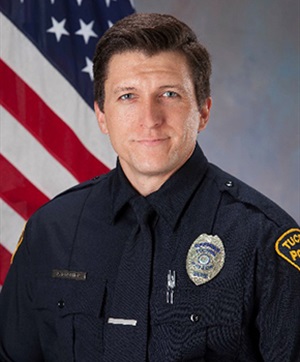 Department photo of a TPD officer in uniform in front of an American flag.